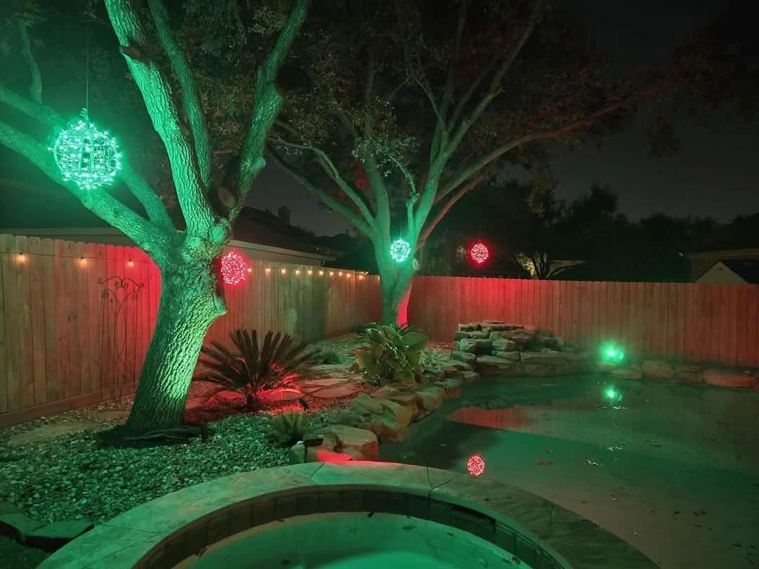 Backyard tree with green and red globe lights over pond