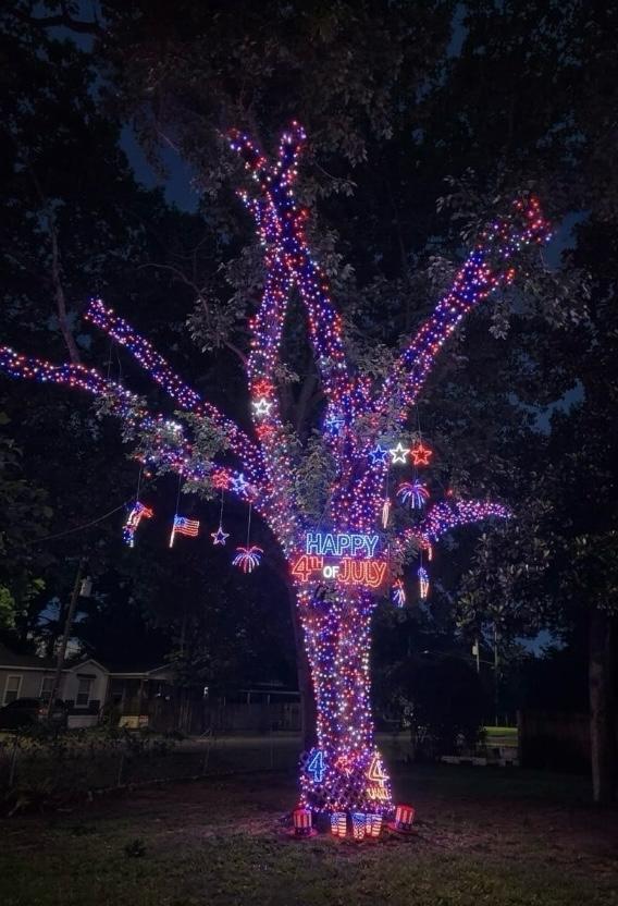 Tree wrapped in red, white and blue LED lights with Happy 4th of July neon sign